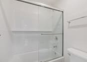 Thumbnail 49 of 51 - A white bathroom with a glass shower door and a white bathtub.