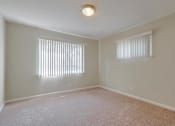 Thumbnail 28 of 37 - A room with a carpeted floor and two windows with blinds.