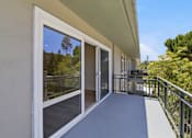 Thumbnail 43 of 92 - A balcony with sliding glass doors leading to a tree-filled landscape.