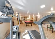 Thumbnail 15 of 42 - A treadmill is in the foreground of a well-lit room with a ping pong table and a green chair.