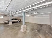 Thumbnail 21 of 42 - A car is parked in a garage with a concrete floor and white ceiling.