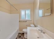 Thumbnail 24 of 29 - A white bathtub sits in a bathroom with a toilet and a window.