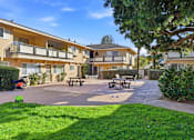 Thumbnail 26 of 33 - A sunny day at a residential complex with a playground and picnic tables.