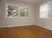 Thumbnail 21 of 22 - A room with wooden floors and white walls has two windows with blinds.