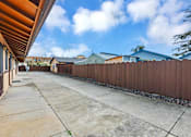 Thumbnail 11 of 38 - A long concrete driveway leads to a house with a brown fence on the side.
