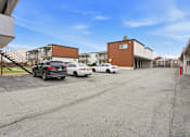 Thumbnail 26 of 55 - A parking lot with cars and buildings in the background.