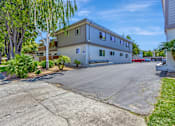 Thumbnail 13 of 41 - A two-story building with a white exterior and a grey roof is surrounded by trees and a driveway.