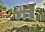 Thumbnail 3 of 27 - A green house with a white door and windows is surrounded by a green lawn.