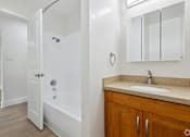 Thumbnail 7 of 10 - A white bathroom with a sink, mirror, and bathtub.