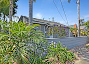 Thumbnail 10 of 31 - A building with a grey roof and a grey wall is surrounded by green plants.
