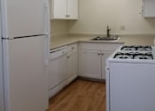 Thumbnail 26 of 33 - A white kitchen with a refrigerator, stove, and cabinets.