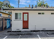 Thumbnail 25 of 31 - A small white house with a red door is situated on a street.