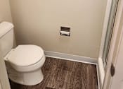 Thumbnail 13 of 42 - A white toilet in a small bathroom with wood flooring.