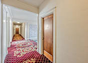 Thumbnail 22 of 42 - A hallway with a red carpet and a wooden door.
