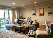 Thumbnail 11 of 22 - A living room with a grey couch, a wooden coffee table, and a chair with a floral pattern.