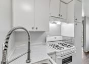 Thumbnail 36 of 40 - A white kitchen with a stove and a hose.