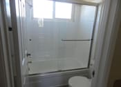 Thumbnail 5 of 14 - A white toilet is in a bathroom with a glass shower door.