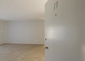 Thumbnail 23 of 29 - an empty living room with a white wall and a door