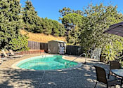 Thumbnail 6 of 8 - A pool surrounded by trees and a fence with a patio table and chairs.