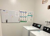 Thumbnail 7 of 8 - A laundry room with a whiteboard and a washer and dryer.