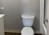 Thumbnail 6 of 10 - A white toilet in a bathroom with a white cabinet and a glass shower door.