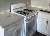 Thumbnail 30 of 33 - A white kitchen with a stove and cabinets.