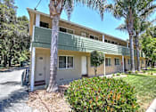 Thumbnail 2 of 20 - A building with a green balcony and a white door is surrounded by trees.