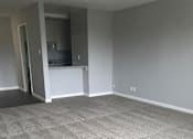 Thumbnail 26 of 30 - A room with a carpeted floor and a kitchen area in the background.