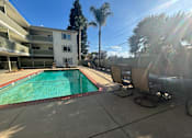Thumbnail 5 of 23 - A pool surrounded by chairs and trees in front of a building.