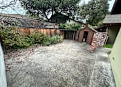 Thumbnail 37 of 38 - A backyard with a concrete slab and a small brick building.