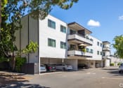 Thumbnail 1 of 16 - a white apartment building with cars parked in front of it