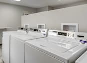 Thumbnail 8 of 15 - A row of white washing machines in a laundromat.