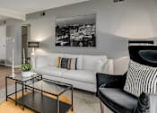 Thumbnail 10 of 15 - A living room with a white couch, a coffee table, and a black and white photo on the wall.