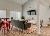 Thumbnail 15 of 15 - A living room with a grey couch, a television, and a wooden floor.
