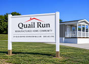 Thumbnail 1 of 6 - A sign for Quail Run Manufactured Home Community with a house in the background.