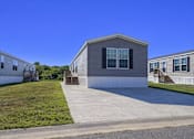 Thumbnail 3 of 6 - A house with a grey siding and a white trim is surrounded by a grassy area and other similar houses.