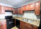 Thumbnail 14 of 20 - A kitchen with black appliances and wooden cabinets at Maplehurst Apartments, Tennessee 37902