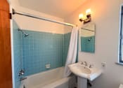 Thumbnail 11 of 12 - A bathroom with a white sink, a white tub, and a blue tile wall.