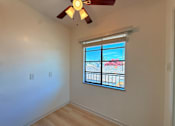 Thumbnail 9 of 12 - A room with a ceiling fan and a window overlooking a balcony.