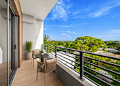 Thumbnail 3 of 21 - A balcony with a table and chairs overlooking a tree-filled landscape.