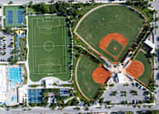 Thumbnail 11 of 21 - An aerial view of a sports complex with a soccer field, baseball diamonds, and a swimming pool.