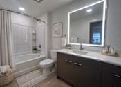Thumbnail 13 of 30 - A bathroom with a white toilet, a sink, and a large mirror.