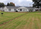 Thumbnail 9 of 12 - A white house with a black roof and a green lawn in front.