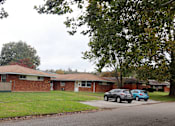 Thumbnail 8 of 12 - A brick house with a car parked in front.