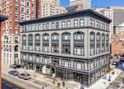 Thumbnail 1 of 20 - A large, old building with many windows is in the middle of a city street.