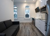 Thumbnail 8 of 20 - A kitchen with a grey couch and wooden floors.