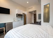 Thumbnail 16 of 20 - A bedroom with a large bed and a kitchen area in the background.