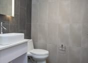 Thumbnail 12 of 20 - A white toilet sits in a bathroom with grey tiled walls.