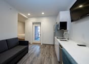 Thumbnail 9 of 20 - A modern kitchen with a grey couch and a wooden floor.