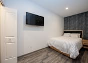 Thumbnail 6 of 20 - A bedroom with a bed, a television, and a door.